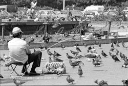 Image du Maroc Professionnelle de  Le Vendeur de mais assis face à l’emblématique fontaine lumineuse de la place Mohammed V, il est presque midi très peu de personne visite cet espace quand le soleil est presque au zénith, le 7 Mars 1987.  Il travaille en groupe avec les photographes de la place leur tactique consiste à  guetter tous ceux qui y affluent dans l’espoir de les convaincre à prendre la pose au milieu des pigeons. (Photo / Abdeljalil Bounhar) 